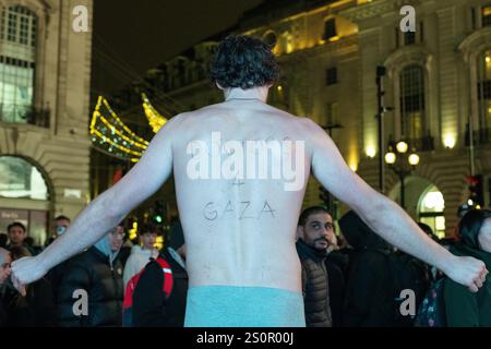 London, Großbritannien. Dezember 2024. In der kalten Nacht im Piccadilly Circus steht ein Mann, der nur in Unterhosen gekleidet ist und auf dem Rücken „Ärzte 4 Gaza“ steht, während palästinensische Unterstützer nach einem israelischen Angriff auf das Kamal Adwan Krankenhaus im Norden Gazastreifens, eine der letzten noch bestehenden Gesundheitseinrichtungen, und der Zwangsräumung von Patienten und medizinischem Personal eine Mahnwache für Gaza veranstalten. Die Demonstranten forderten einen Waffenstillstand, dringende medizinische Hilfe und Rechenschaftspflicht für Verstöße gegen das Völkerrecht. Quelle: Ron Fassbender/Alamy Live News Stockfoto