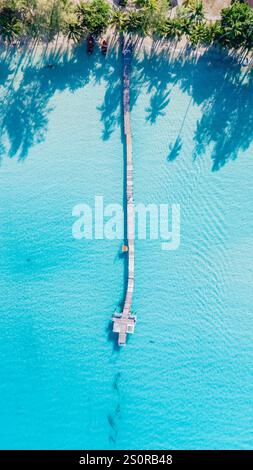 Helles türkisfarbenes Wasser erstreckt sich endlos, hervorgehoben durch den atemberaubenden Holzpier, der zum Horizont reicht. Stockfoto