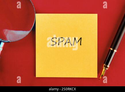 Eine hellgelbe Haftnotiz mit dem Wort Spam wird auf einer roten Oberfläche platziert, begleitet von einer Lupe und einem Stift, um die Bedenken in Digitala hervorzuheben Stockfoto