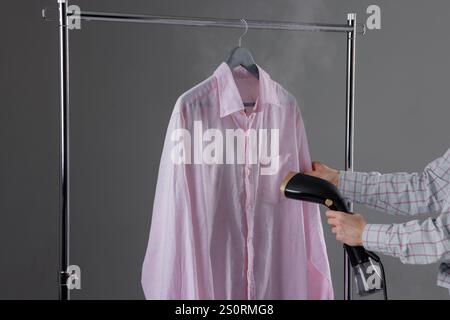 Frau, die Kleidung zu Hause auf einem Kleiderbügel dampfen, Nahaufnahme, Handdampfer in der Hand der Frau. Stockfoto