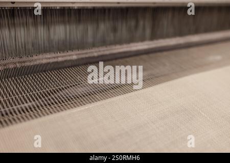 Garnfäden auf der Webmaschine. Eine Webmaschine für Kleidung oder gewebte Etiketten. Webmaschine für die Bekleidungsindustrie. Webstuhl in Texti Stockfoto