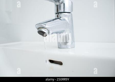 Nahaufnahme einer Armatur im Badezimmer mit fließendem Wasser und Kalkflecken und schmutzigem Waschbecken Stockfoto