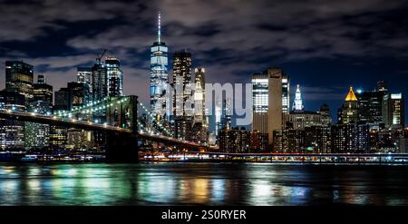 Ein atemberaubender Blick auf die Skyline von New York City mit beleuchteten Wolkenkratzern und der Brooklyn Bridge über den East River mit Reflexionen Stockfoto