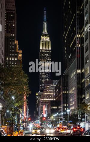 Ein nächtlicher Blick auf das Empire State Building, beleuchtet vor einem dunklen Himmel, umgeben von Stadtgebäuden und belebtem Verkehr auf der Straße darunter. Stockfoto
