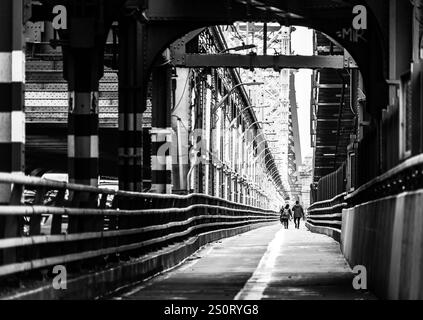 Ein Schwarzweiß-Foto, das einen langen, leeren Gang unter einer Brücke aufnimmt. Die Perspektive führt zu zwei Figuren, die in der Ferne laufen, gerahmt Stockfoto