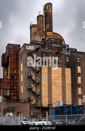 Ein verlassenes Industriebau mit rostigen Strukturen und Graffiti. Das Gebäude verfügt über mehrere Stockwerke, Feuerleiter und große Schornsteine. Die Stockfoto