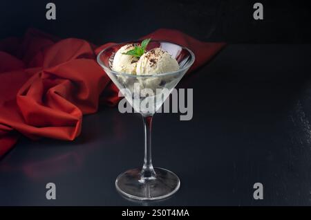 Eis mit Schokolade in einem Martini-Glas und Minze auf schwarzem Hintergrund. Kreatives minimalistisches Konzept. Auf dunklem Steingrund. Stockfoto