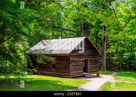 Eine kleine, alte Blockhütte befindet sich in einem bewaldeten Gebiet. Die Hütte ist von Bäumen umgeben und hat ein Schindeldach. Die Hütte scheint verlassen zu sein, ohne jemanden Stockfoto