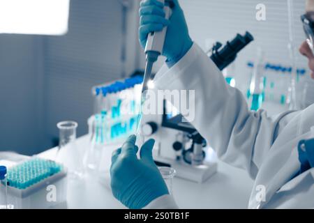 Ein erfahrener Laborwissenschaftler verwendet fachmännisch eine Pipette, ein wichtiges Werkzeug für die präzise Handhabung von Flüssigkeiten in Experimenten, um genaue Messungen zu gewährleisten Stockfoto