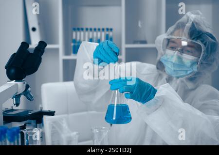 Ein engagierter Wissenschaftler führt im Rahmen seiner laufenden Forschung ein akribisches Laborexperiment mit einer leuchtend blauen Lösung durch Stockfoto