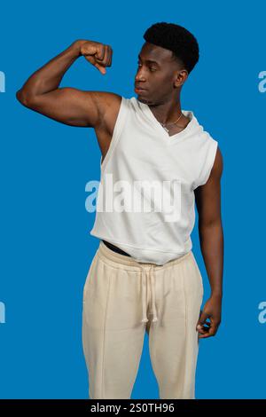 Sportlicher Mann, der seinen Bizeps beugt, zeigt Kraft und Fitness vor einem leuchtend blauen Hintergrund Stockfoto