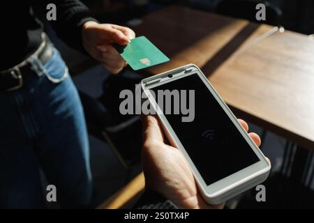 Ein Mann akzeptiert Zahlungen von einem Kunden über ein Kreditkartenterminal in einem Geschäft oder Café. Stockfoto