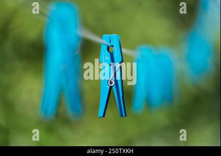 Nahaufnahme eines blauen Kleiderschachts, der draußen an einer Wäscheleine hängt, mit einem unscharfen grünen Hintergrund. Stockfoto