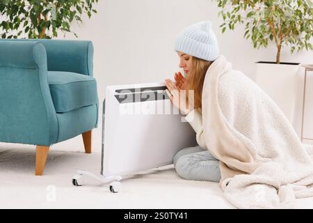 Gefrorene junge Frau mit karierter Wärme in der Nähe des Heizkörpers zu Hause. Stockfoto