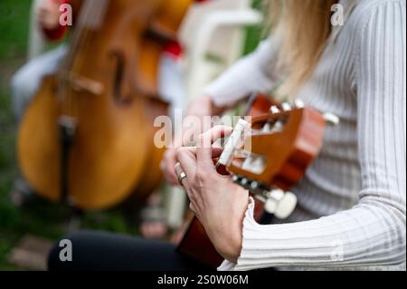 Eine Nahaufnahme der Hände, die eine akustische Gitarre spielen, mit einem verschwommenen Hintergrund, der ein Cello zeigt, das gespielt wird, und die Essenz eines musikalischen Moments im Outdo erfasst Stockfoto