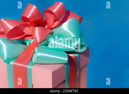 Ein Geschenk mit einem schönen Band. Die rosafarbene Box ist mit grünen und karmesinroten Bändern auf dem Hintergrund des Pools dekoriert. Platz für Text. Stockfoto