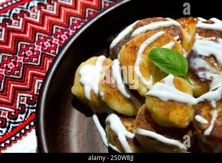 Käsekuchen in Sauerrahm auf einer Keramikplatte. Nahaufnahme des Hintergrunds von Handtüchern mit Ornament. Stockfoto
