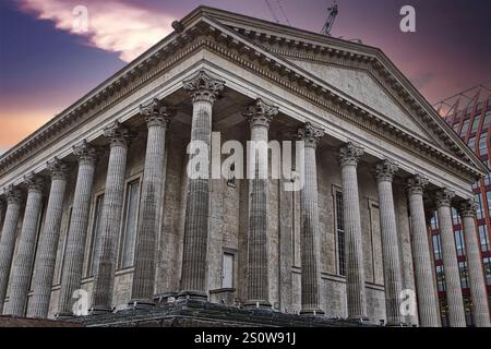 Ein flacher Blick auf ein klassisches Gebäude mit zahlreichen großen grauen Säulen und komplizierten Mauerwerken vor einem Dämmerhimmel. Ein modernes B Stockfoto