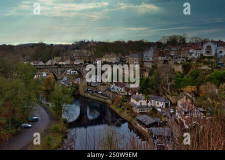 Steinviadukte über einem Fluss, neben einer Stadt mit Häusern und Bäumen unter bewölktem Himmel. Autos sind auf einer Straße unterhalb des Viadukts in Knaresborou zu sehen Stockfoto