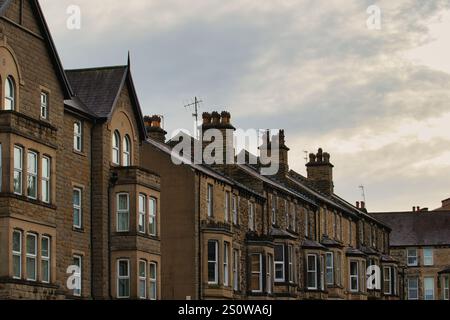 Eine Reihe von Reihenhäusern, überwiegend brauner Stein, mit unterschiedlicher Anzahl von Fenstern und Schornsteinen, unter bewölktem Himmel. Der architektonische Stil ist konstant Stockfoto