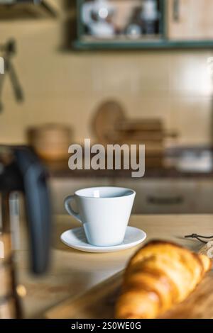 Frühstück in der Küche mit frisch zubereitetem Croissant und einer Tasse heißem Kaffee, Kaffeemaschine, Croissant und Küche außer Fokus, früh aufwachen zu Hause Stockfoto