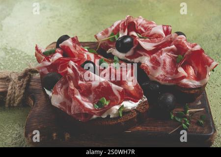 Geräucherter Schinken, Sandwiches mit Schinken und schwarzen Oliven, italienisches Gericht, Delikatesse, Parmaschinken, Frühstück, Draufsicht, keine Leute Stockfoto