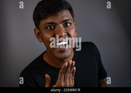 Ein junger Mann mit einem überraschten und leicht schelmischen Ausdruck, der mit der Hand Gesten macht. Stockfoto