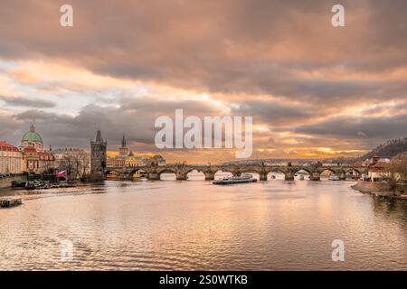 Prag, Tschechische Republik - 20. Dezember 2024: Landschaft auf der Moldau mit Karlsbrücke mit Altstadtturm mit Touristenboot unter farbenfrohem Sonnenuntergang Stockfoto