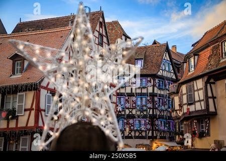 Verwischtes Weihnachtssternornament auf dem Weihnachtsmarkt in Colmar, Frankreich, mit verzierten, halbfachwerkgerahmten Häusern im Hintergrund Stockfoto