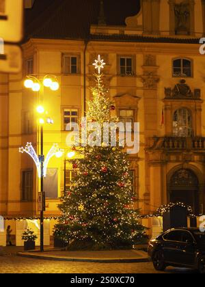 Beleuchteter Weihnachtsbaum vor dem kunstvollen Gebäude mit Straßenlaternen und dekorativen Lichtern in Prag Stockfoto