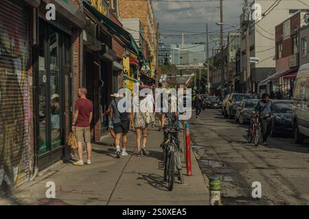 Toronto, ON, Kanada - 21. September 2024: Fußgänger schlendern durch eine geschäftige Stadtstraße, die von Geschäften und Fahrrädern gesäumt ist. Stockfoto