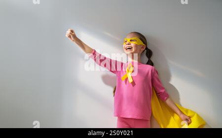 Weltkinderkrebstag. Mädchen im Superhelden Kostüm mit goldenem Band. Stockfoto