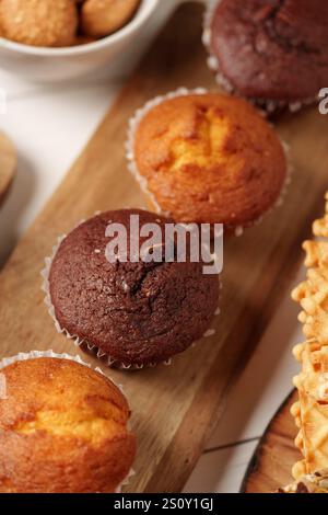 Frisch gebackene Muffins auf einem Holzbrett mit verschiedenen Snacks für einen gemütlichen Nachmittagsgenuss Stockfoto