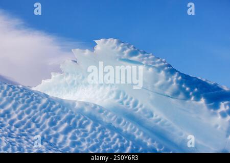 Gezacktes Randdetail eines blauen Eisbergs vor blauem Himmel und Wolkenhintergrund. Kjerulf Fjord, Nordost-Grönland-Nationalpark. Leerzeichen für Text. Stockfoto