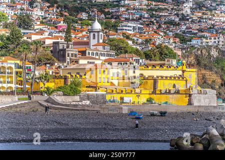 Farbenfrohe Küstenszene mit einer gelben Festung am Meer, umgeben von lebhaften Dorfhäusern. Stockfoto