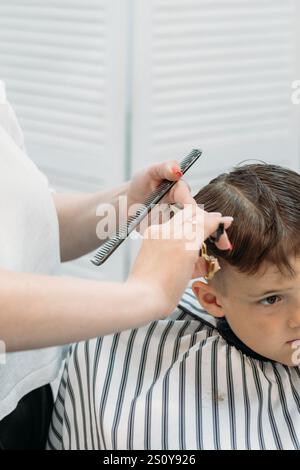 Eine Friseurin schneidet einem kleinen Jungen mit Kamm und Schere die Haare Stockfoto