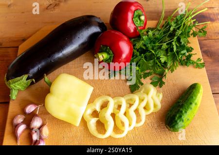 Buntes Gemüse, einschließlich Auberginen, Paprika und Gurken, wird ordentlich geschnitten und auf einem hölzernen Schneidebrett angeordnet, fertig zum Kochen oder Salatvorbereitung Stockfoto
