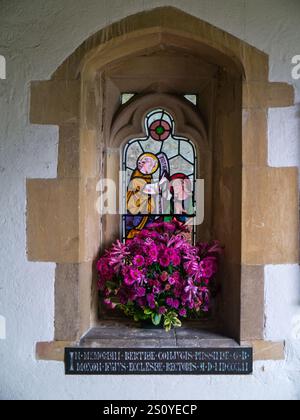 Auf der Veranda der Kirche St. Mary Magdalene, Sandringham, Norfolk, Großbritannien; Buntglasfenster mit einer Vase mit frischen Blumen davor Stockfoto