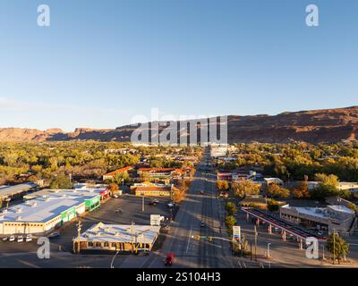 Blick aus der Vogelperspektive über Moab, Utah, USA und die Hauptstraße bei Sonnenuntergang, mit den markanten Klippen und den La Sal Bergketten, die die Stadt umgeben. Stockfoto