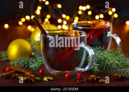 Zwei Gläser mit heißem Glühwein mit Orange und Gewürzen auf einem Holzhintergrund mit weihnachtsdekorationen vor dem Hintergrund festlicher Lichter. Tr Stockfoto