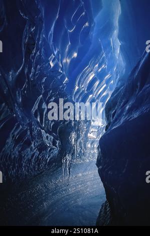 Eishöhle in der Antarktis. Blaue Höhle mit Eisformationen und einem kleinen Wasserstrom. Die Höhle ist dunkel und kalt, aber die blaue Farbe von Eis und Wasser Stockfoto