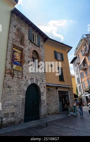 Ein historisches Steingebäude mit einer großen bogenförmigen grünen Tür und einem religiösen Wandgemälde an der Mauer, in einer engen Kopfsteinpflasterstraße gelegen. Stockfoto