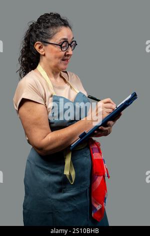 Lächelnde Kellnerin, die eine Bestellung mit Stift und Notizblock entgegennimmt, Schürze und Brille trägt und im Restaurant arbeitet Stockfoto