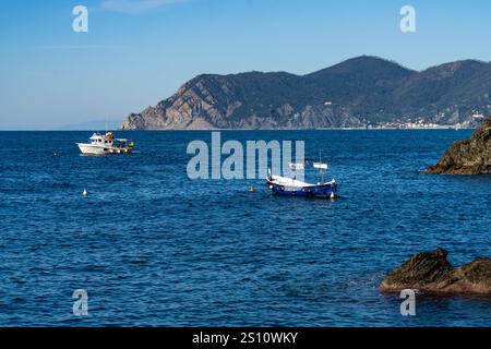 Fischerboote vor der zerklüfteten Küste der Cinque Terre Stadt Manarola, Italien. In der Ferne befindet sich die Stadt Monterosso al Mare. Stockfoto