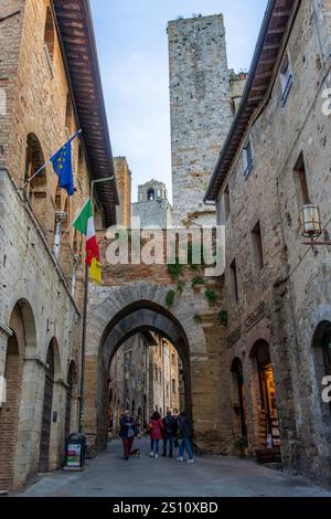 Touristen auf der Via San Matteo in der Nähe des Chancellery Tores in der mittelalterlichen Stadt San Gimignano, Italien. Dahinter befinden sich Torre Rognosa & Torre Salvucci. Stockfoto