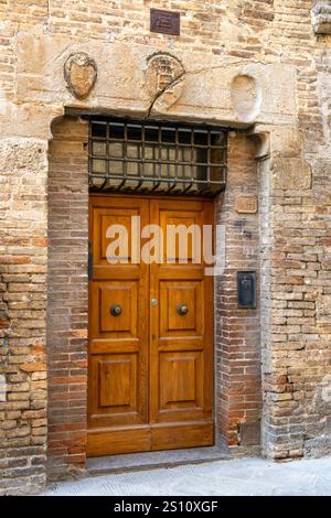 Eine Holztür und alte Steinschnitzereien an der Via San Giovanni in der ummauerten Stadt San Gimignano, Italien. Stockfoto