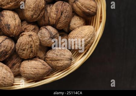 Walnüsse in einem Korb auf dunklem hölzernem Hintergrund. Nüsse in einem ovalen Korb, Draufsicht. Haufen Walnüsse in Muscheln, Nahaufnahme, Hintergrund. Gesunde Ernährung Stockfoto