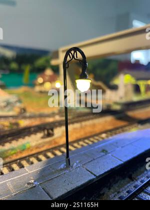 Ein wunderschön detaillierter Bahnhofsbahnsteig mit einer Straßenlaterne im Vintage-Stil, die mit warmem Licht beleuchtet wird. Modelleisenbahn-Layout. Stockfoto