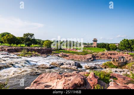 Sioux Falls, SD USA - 26. August 2017: Malerischer Blick auf Wasserfälle, die über roten Granit und historische Pferdescheune im Falls Park in South Dakota kaskadieren. Stockfoto