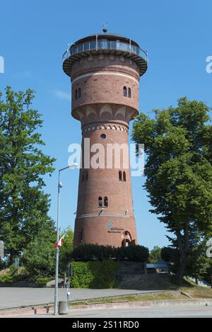 Ein hoher Backsteinwasserturm neben grünen Bäumen unter blauem Himmel, Museum und Café, Wasserturm, Gizycko, Warminsko-Mazurskie, Warminsko-Mazurskie, Polen Stockfoto